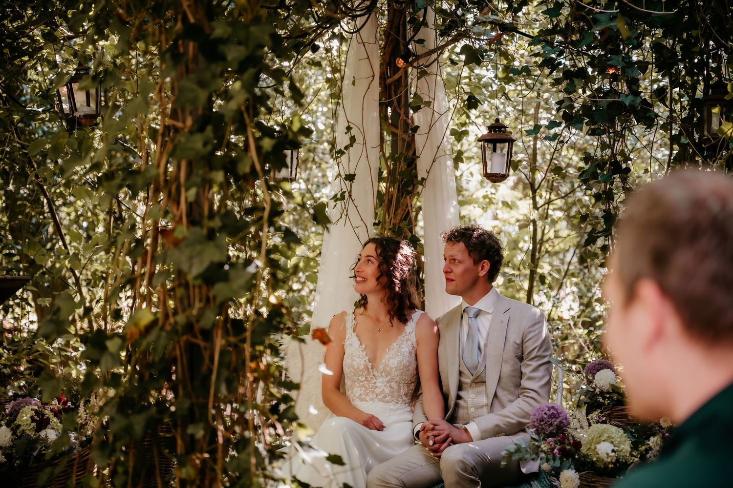 Outdoor wedding ceremony under tree canopy with dappled sunlight.