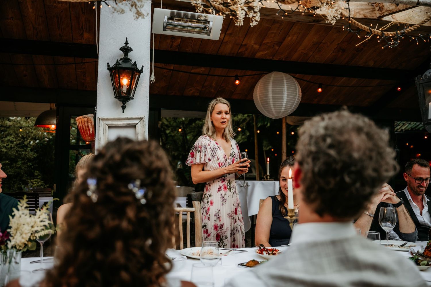Wedding reception dinner scene with elegant table settings and hanging lantern decor.
