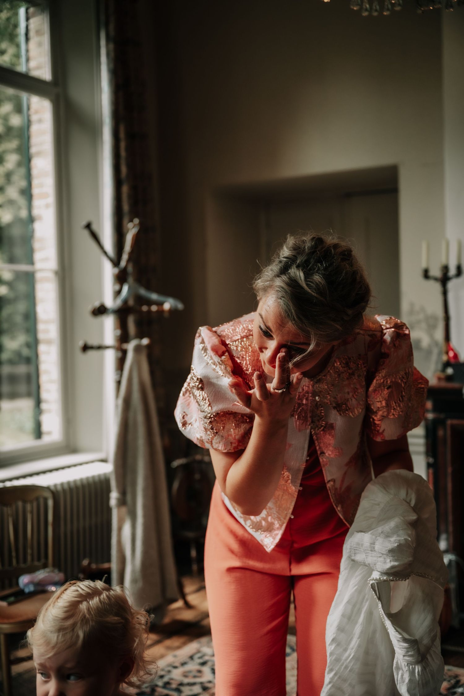 Wedding preparation scene with pink and white dresses in a bright room with windows.
