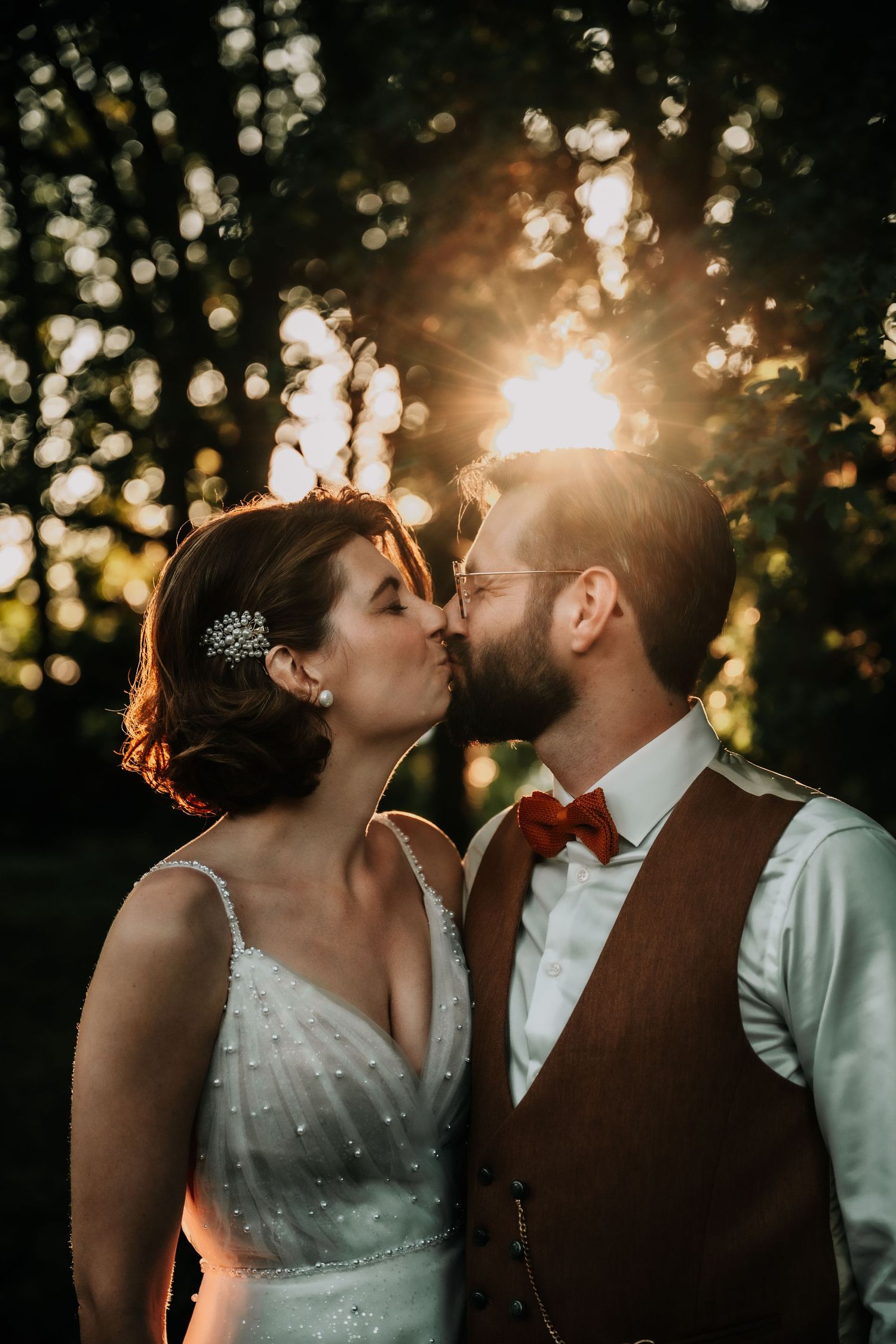 Wedding couple shares a romantic kiss at sunset with golden bokeh lights in the background.