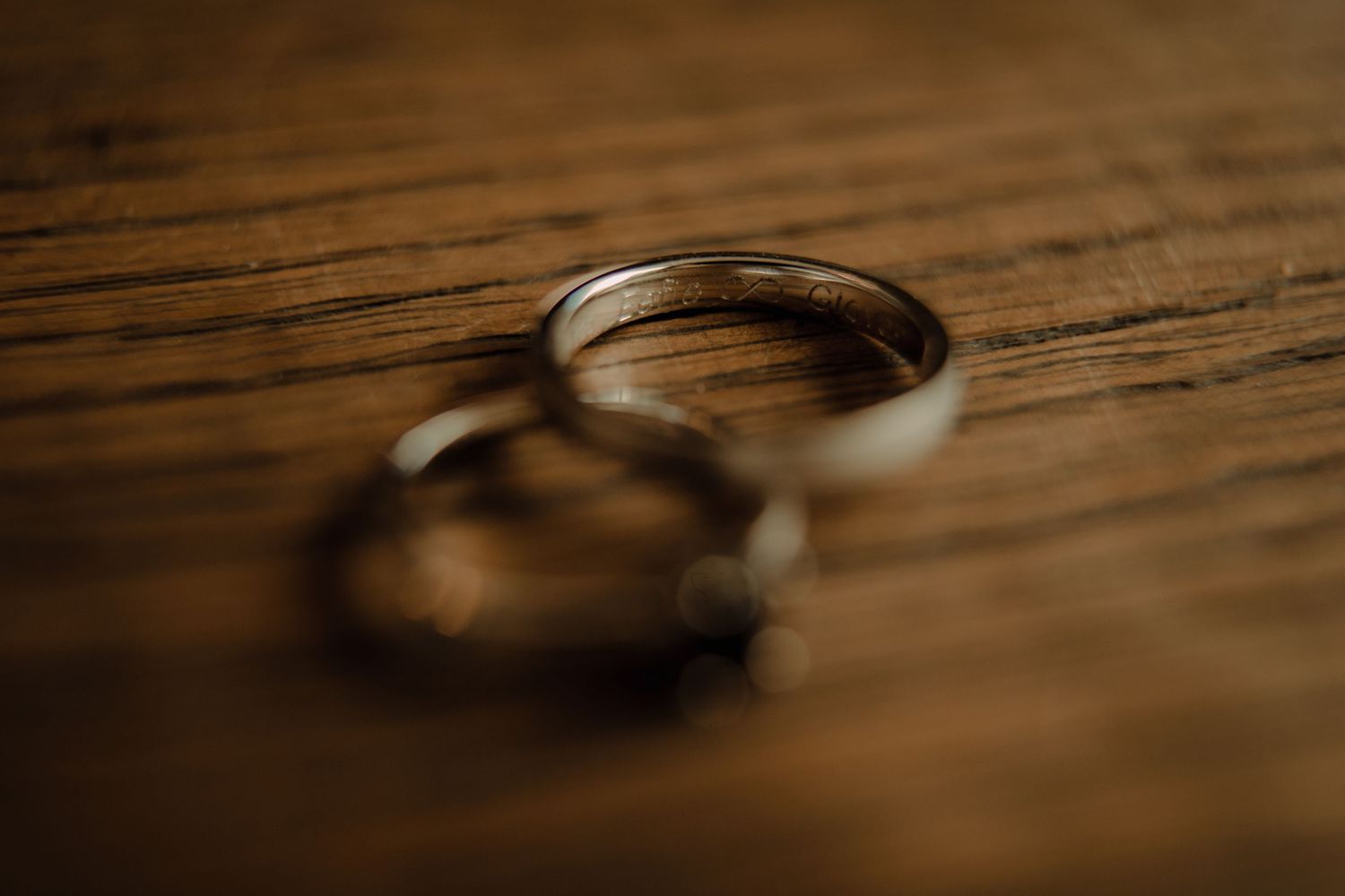 Two wedding rings casting shadows on rustic wooden surface in warm lighting.