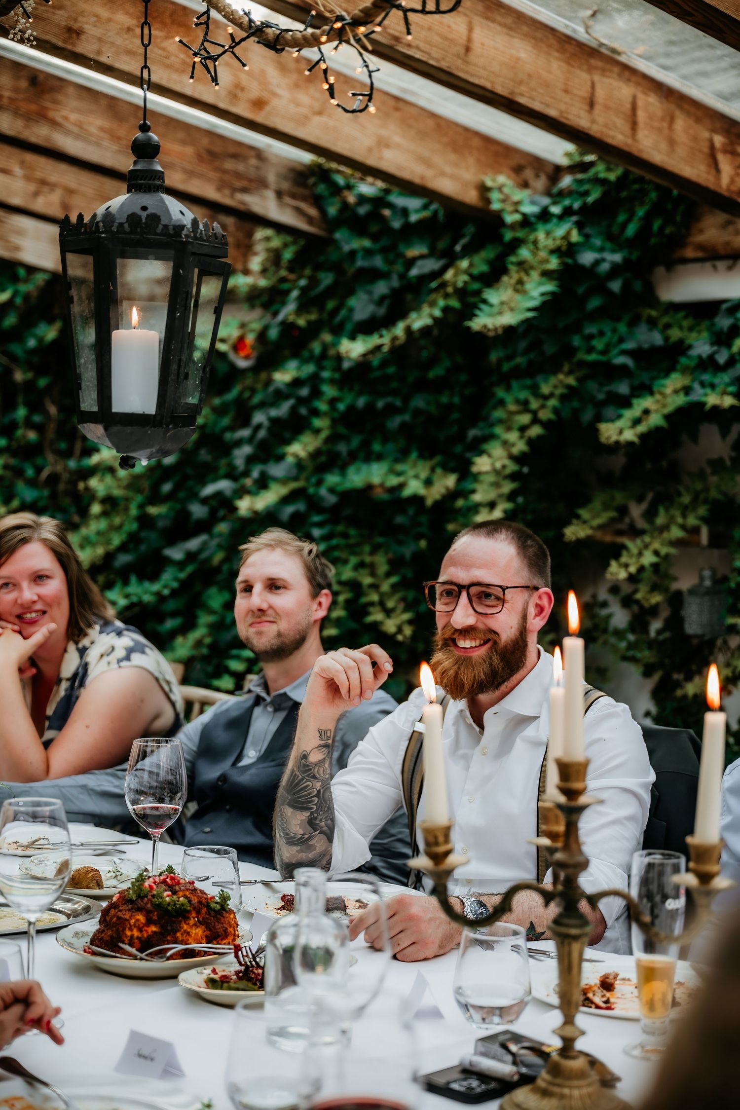 Wedding reception dinner with guests seated at a long table under rustic wooden beams.