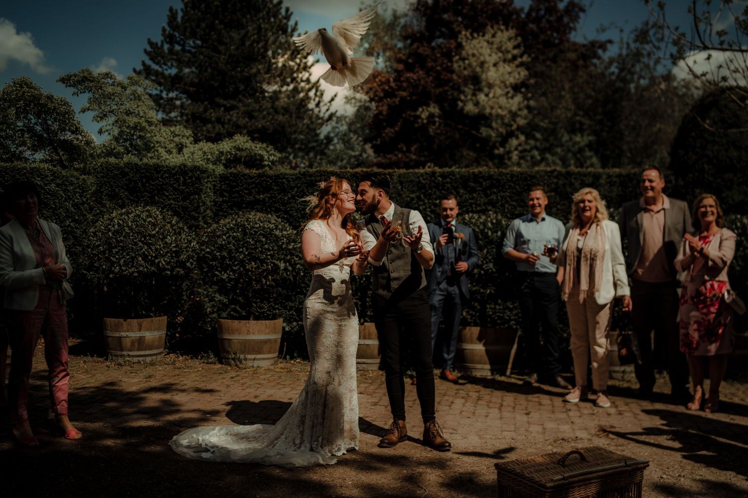 An outdoor wedding ceremony taking place in a garden setting with guests watching the celebration.