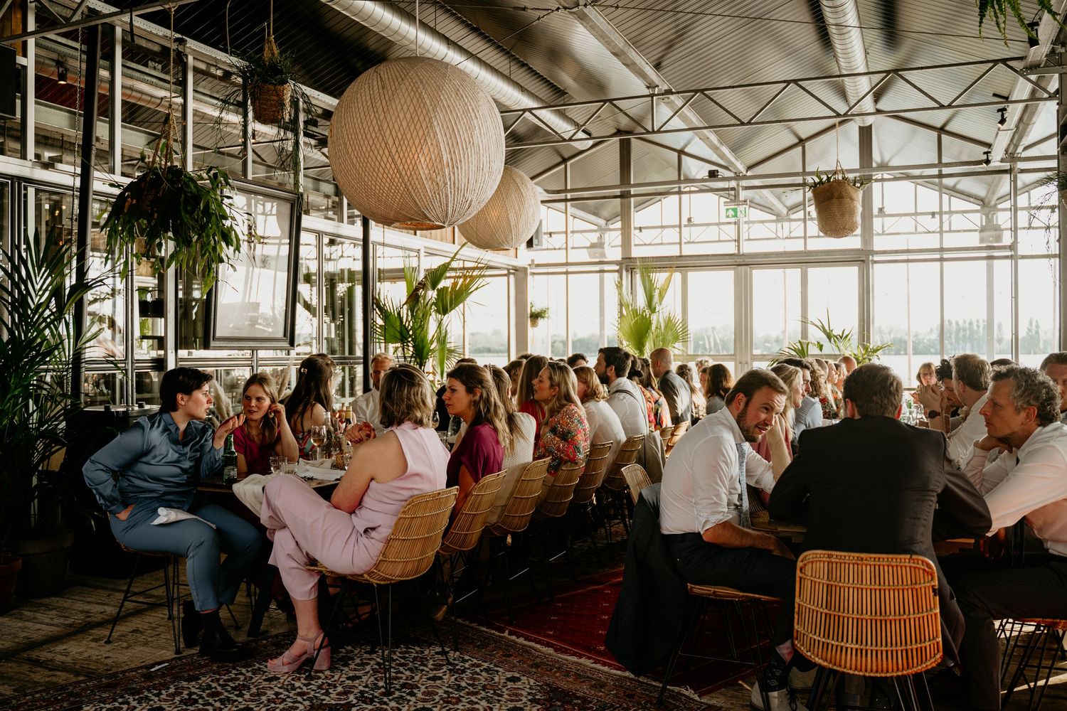 Large group dining in bright modern restaurant with industrial ceiling and hanging pendant lights.