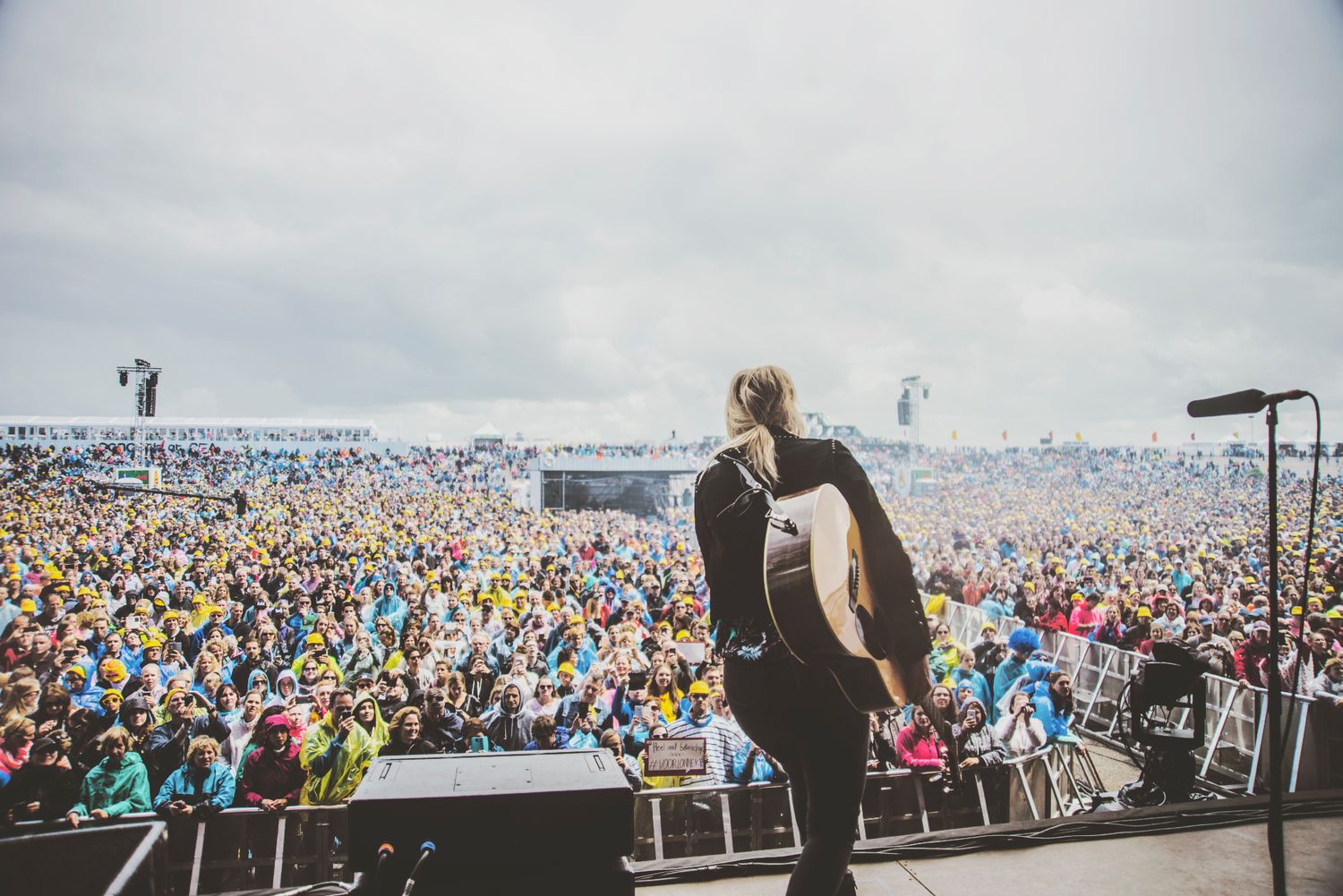 A massive crowd of festival attendees fills the outdoor venue grounds during a live music performance.