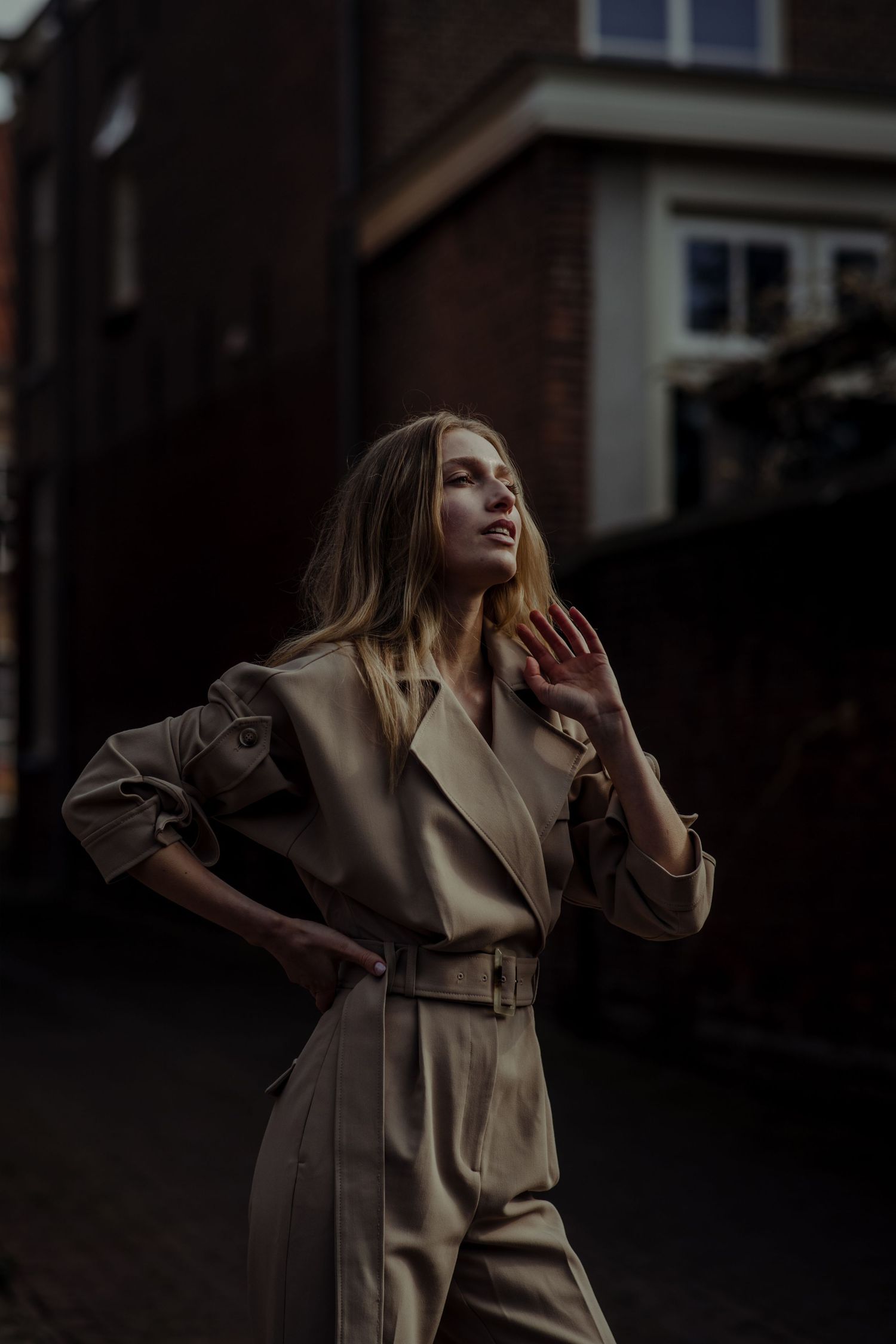 A woman in a beige trench coat poses dramatically in a series of moody fashion photographs.
