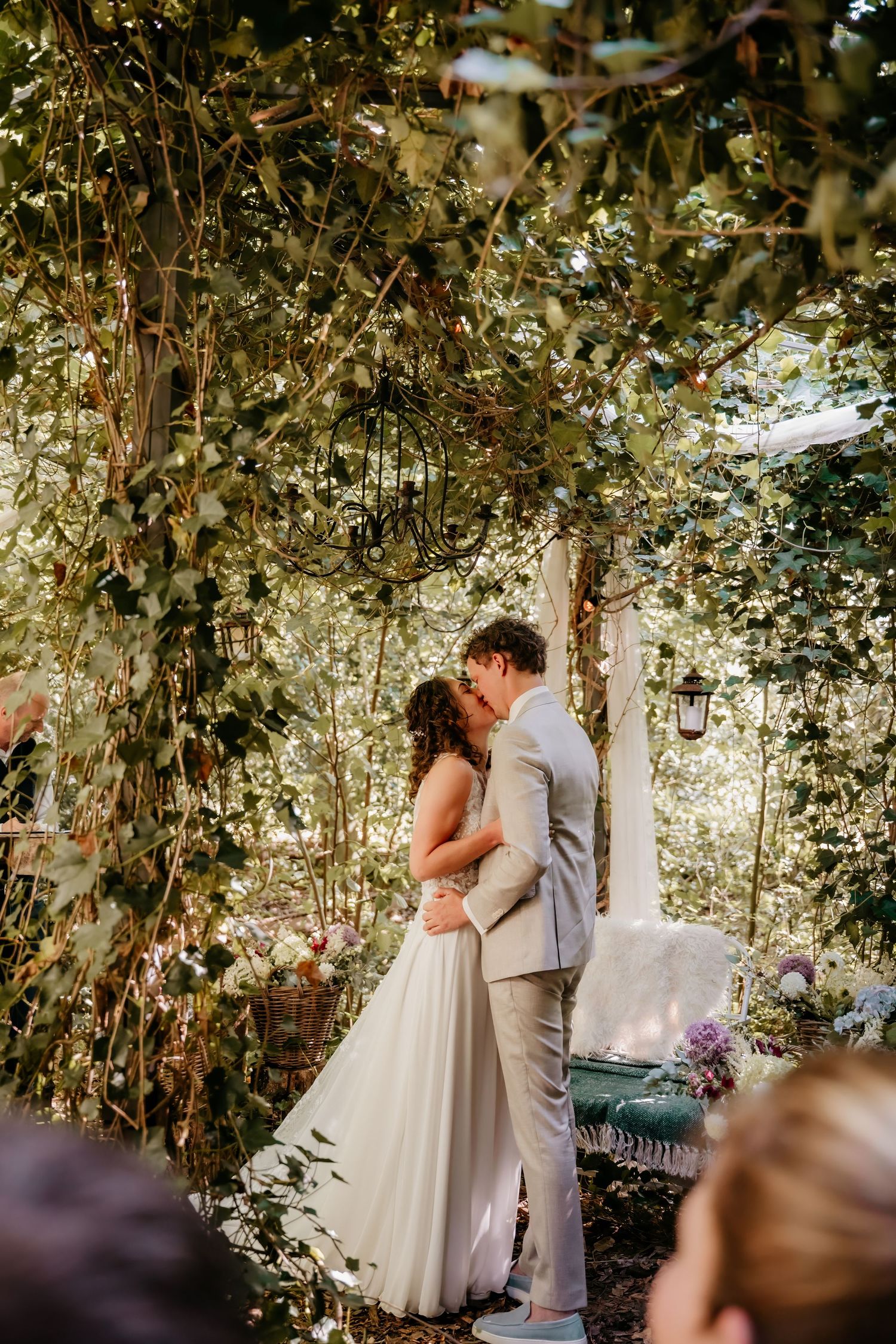 Romantic wedding moment captured in enchanted garden setting with climbing vines and lanterns.