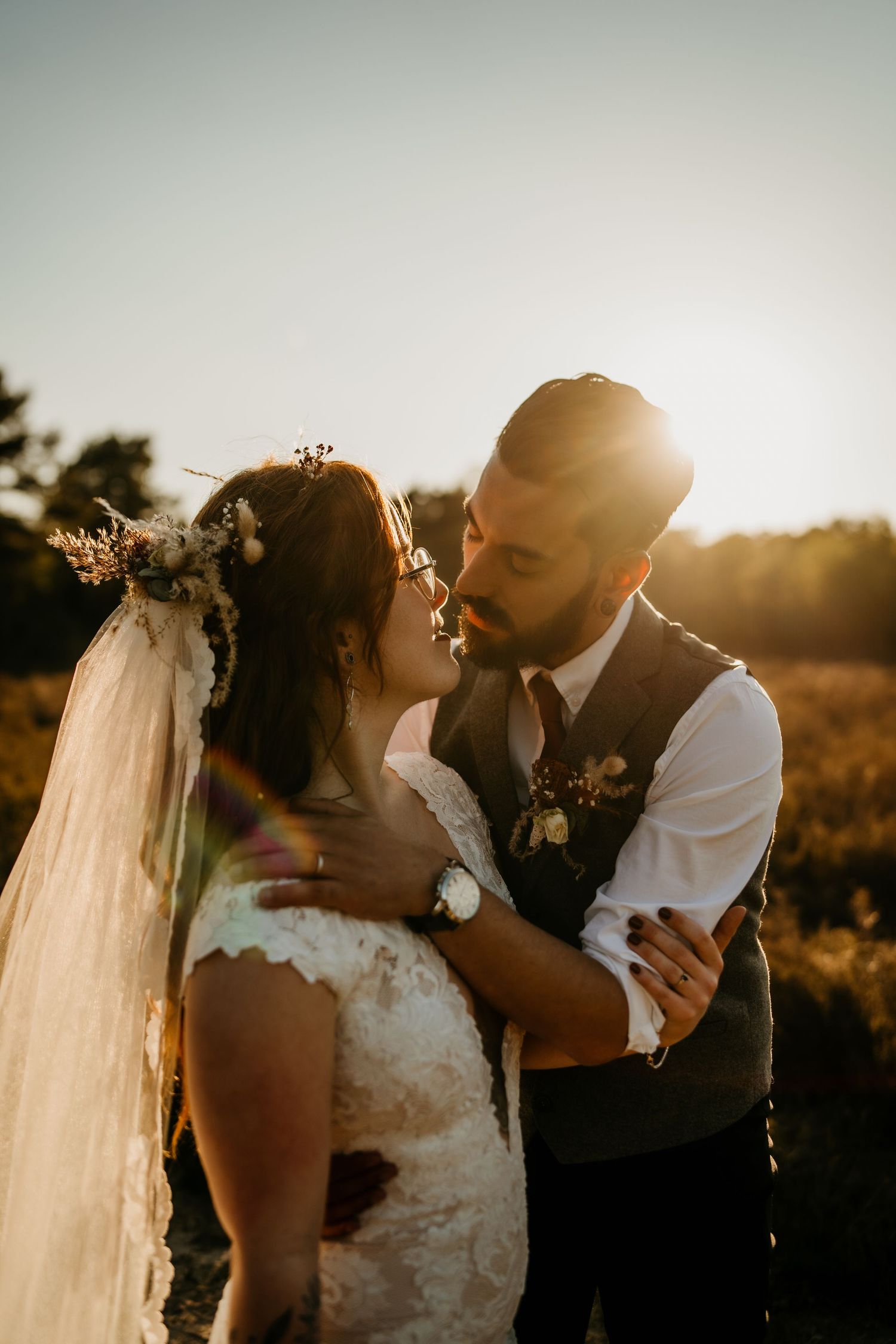 Couple embracing in golden sunlight during sunset at outdoor wedding celebration.