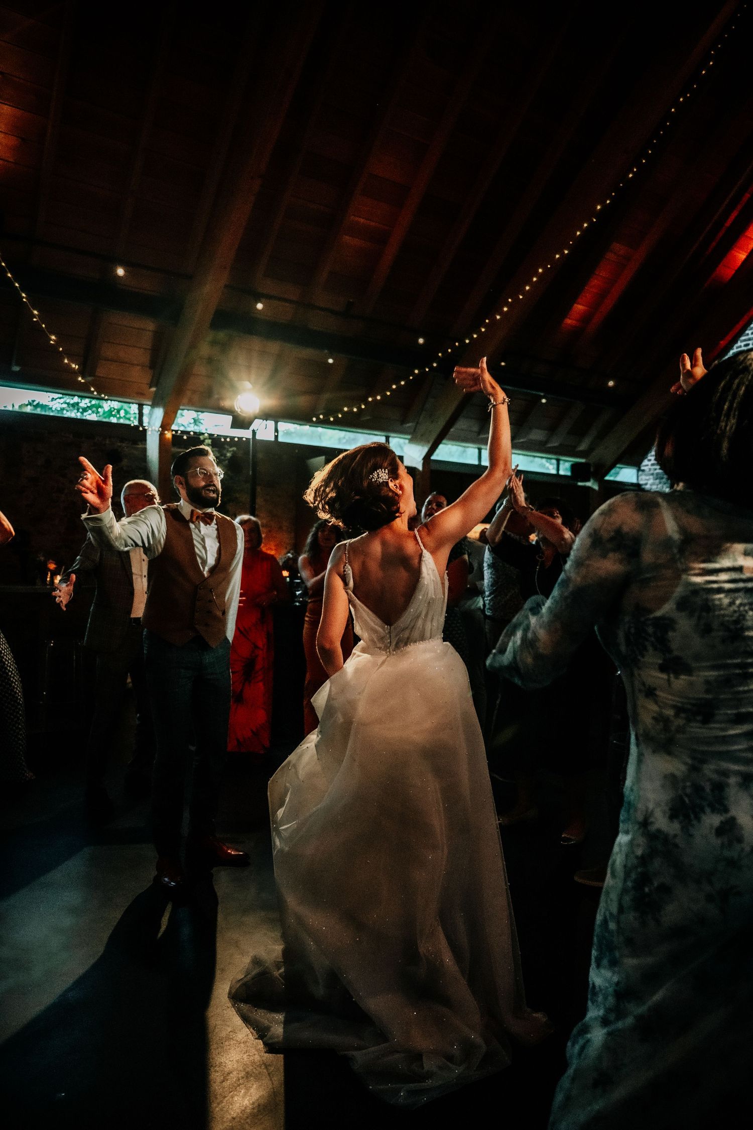 Silhouettes of people dancing at a reception under moody lighting and string lights.