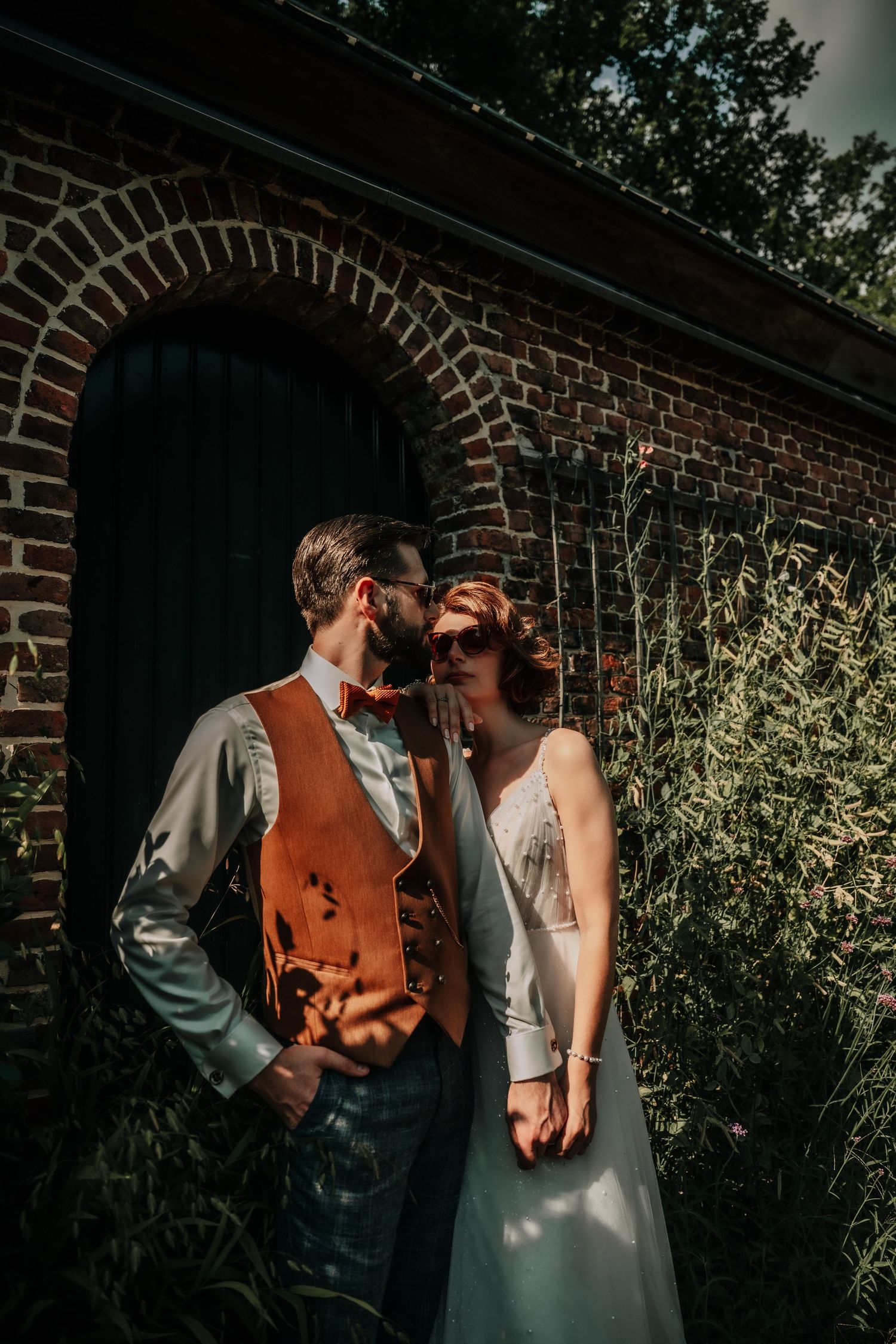 A romantic moment between newlyweds against a rustic brick wall with natural lighting.