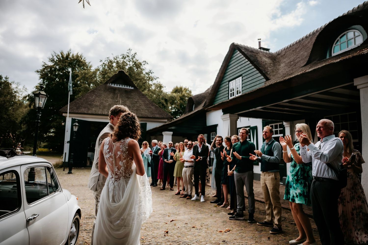Wedding guests line up outside a rustic venue to celebrate the newlyweds.