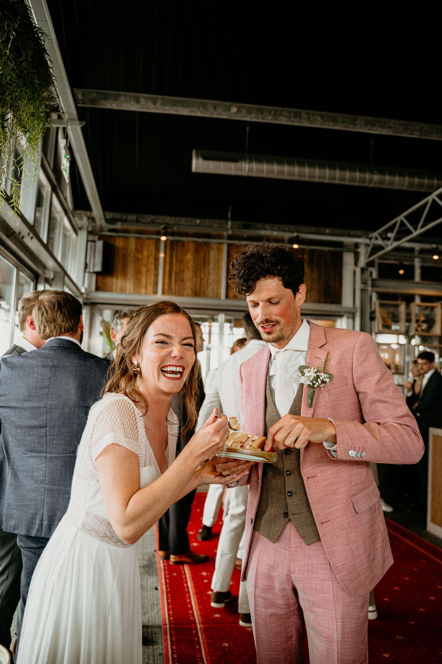 A couple shares a joyful moment while eating at their wedding reception in an industrial-style venue.