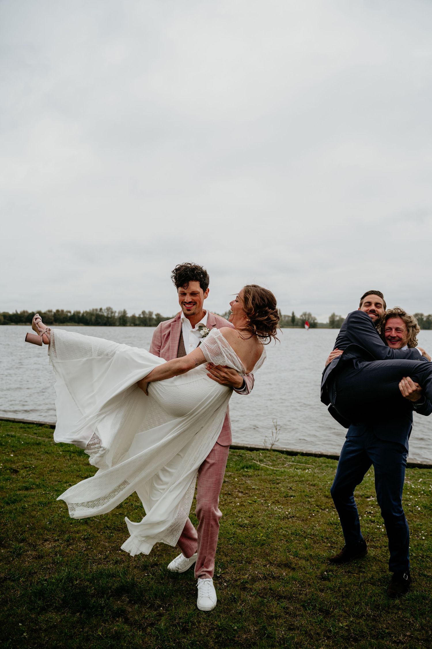 A playful sequence shows a couple in wedding attire dancing and spinning together by a lake on an overcast day.