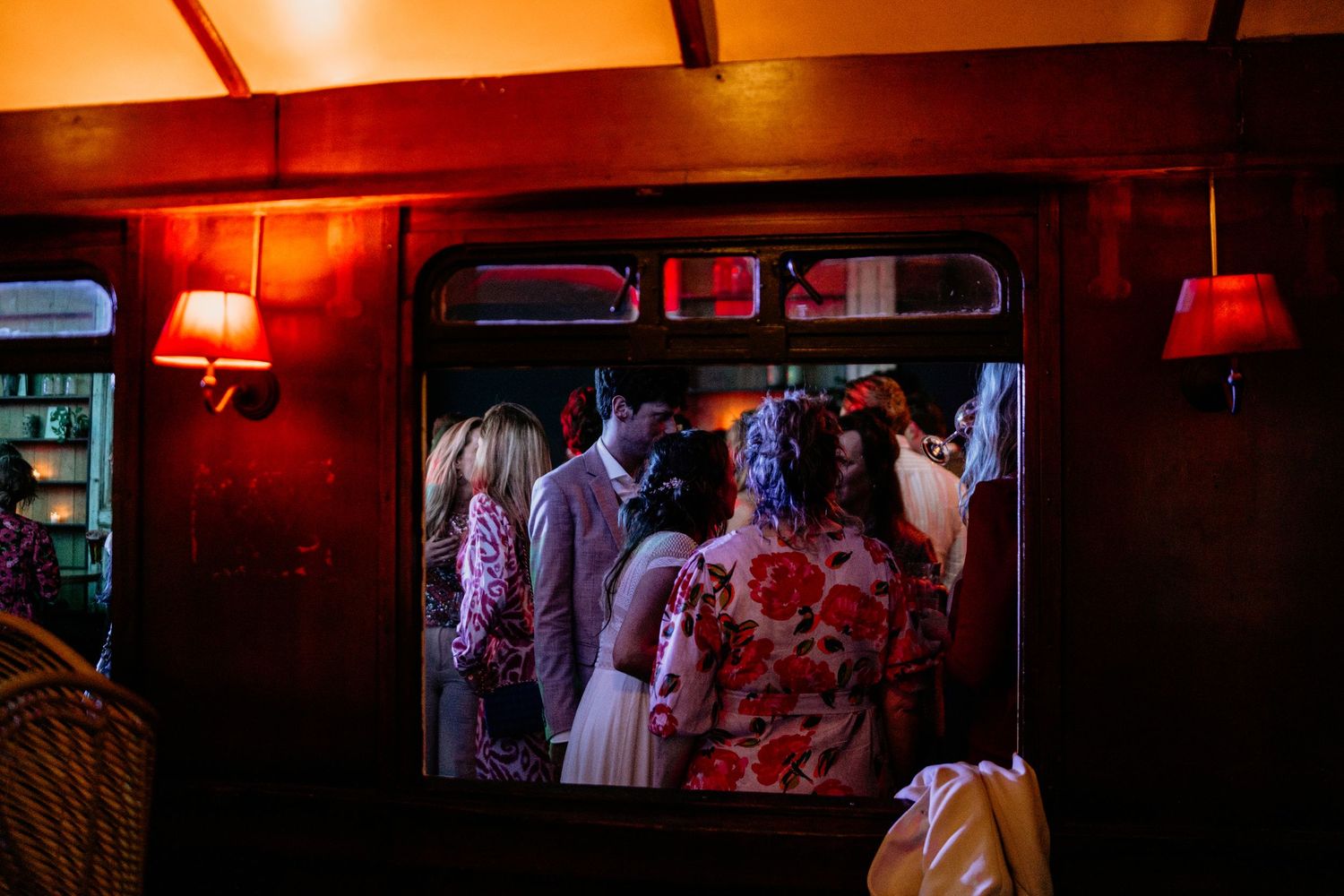 Crowd of party guests seen through doorway under warm red lighting.