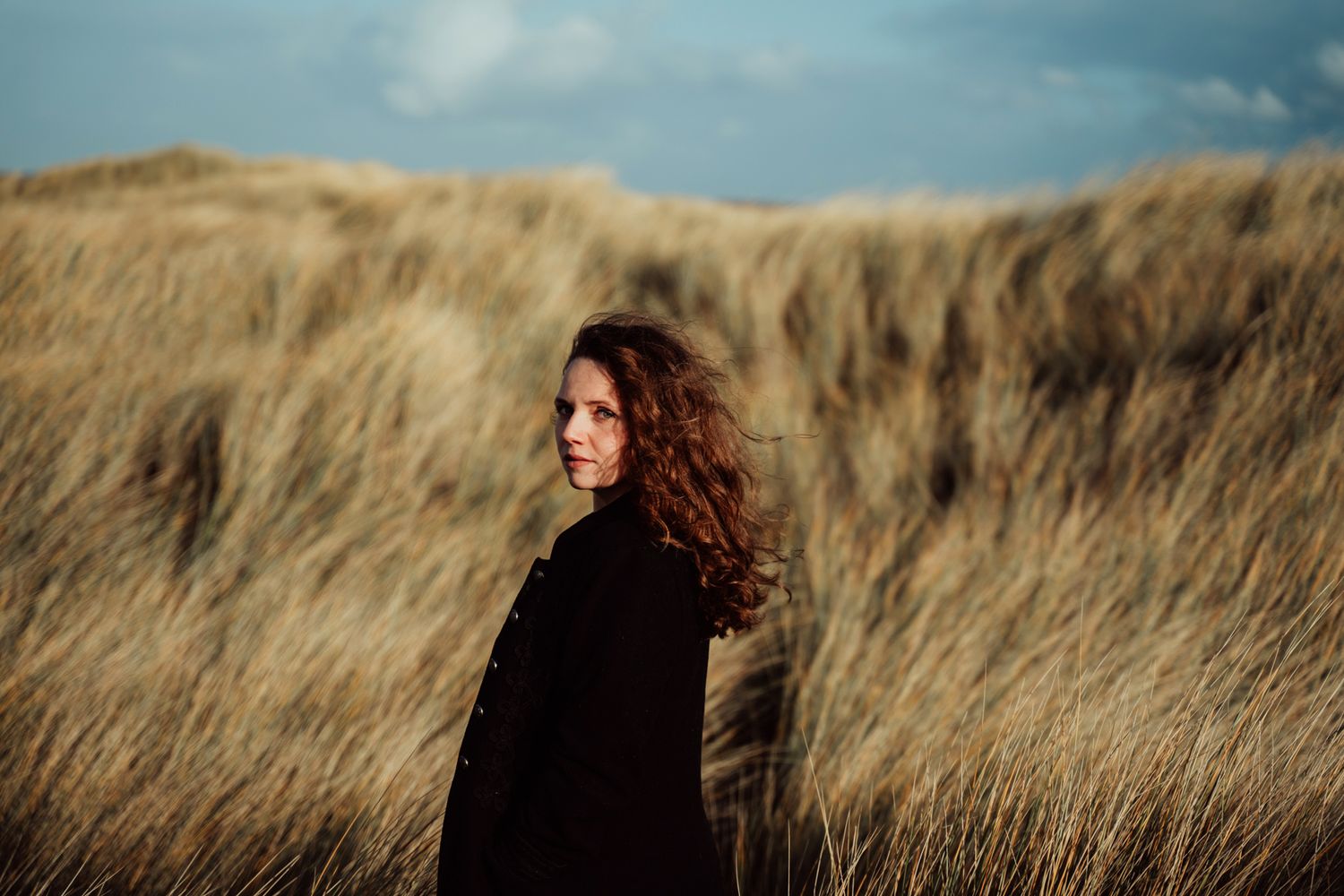Silhouette of a person with flowing hair stands in golden wheat field against moody cloudy sky at sunset.