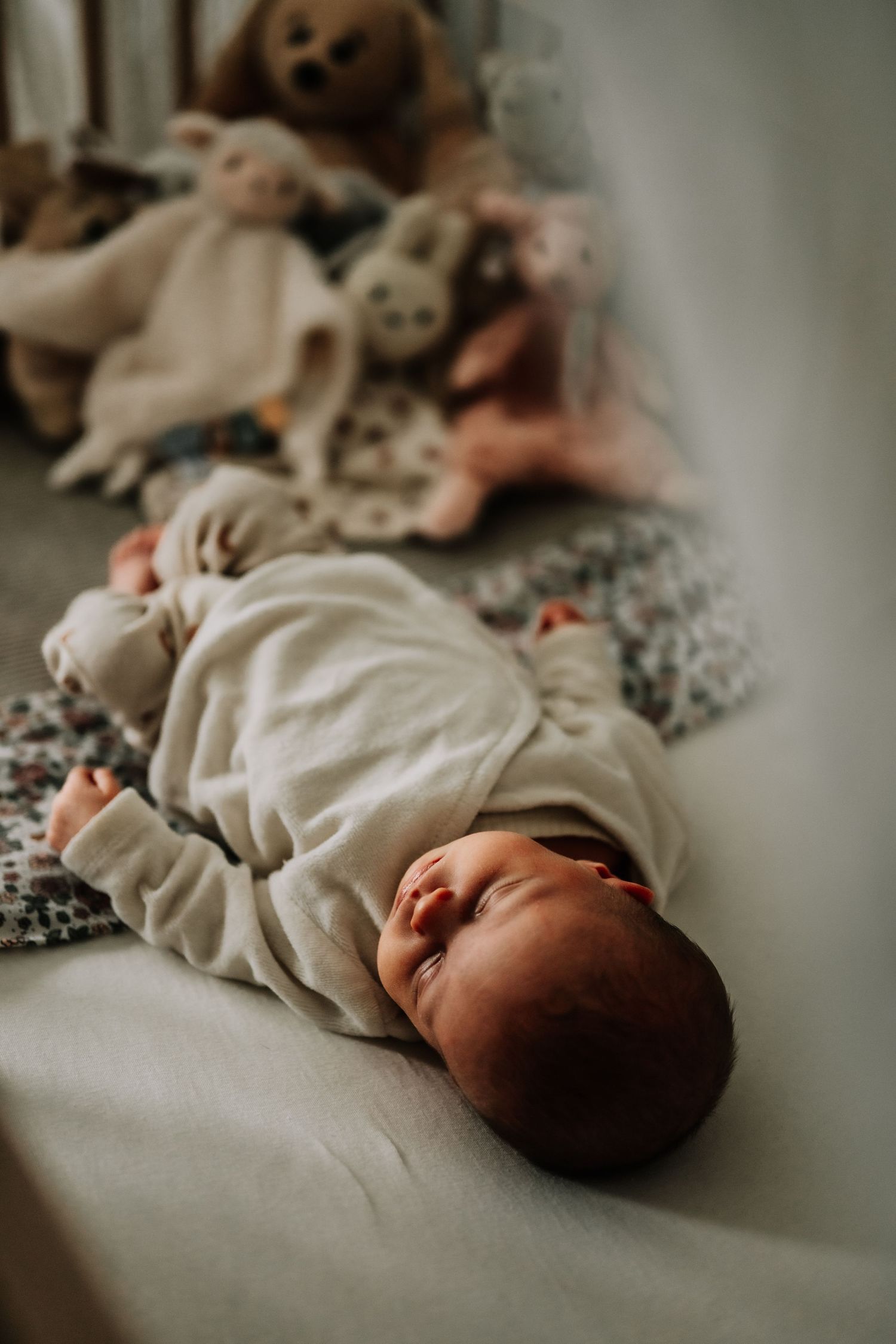 Baby resting on floral bedding surrounded by plush stuffed animals in a crib.