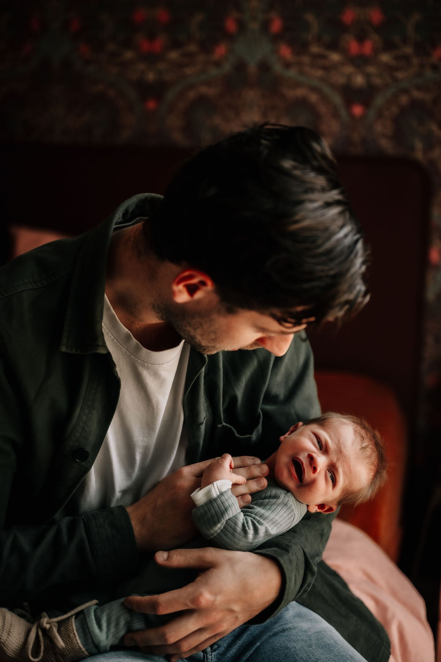 Intimate moment with a newborn baby against a backdrop of vintage red wallpaper.
