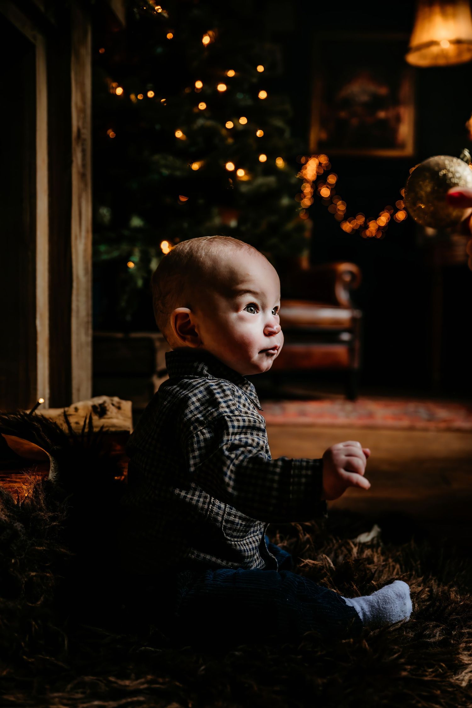 A baby sits on the ground at dusk with twinkling lights in the background creating a moody atmosphere.