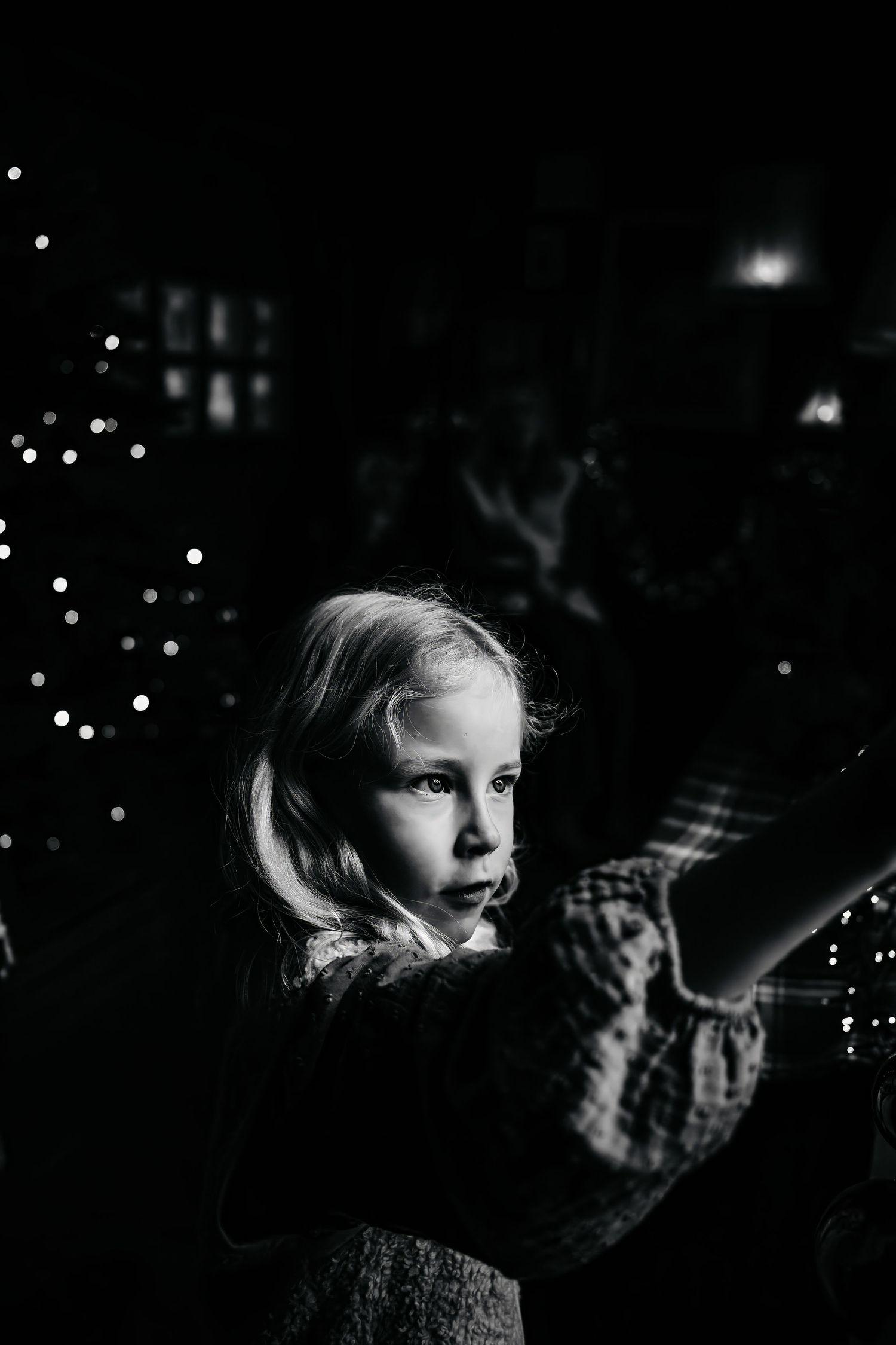 A series of dark atmospheric black and white photographs showing a child gazing at twinkling lights in the darkness.