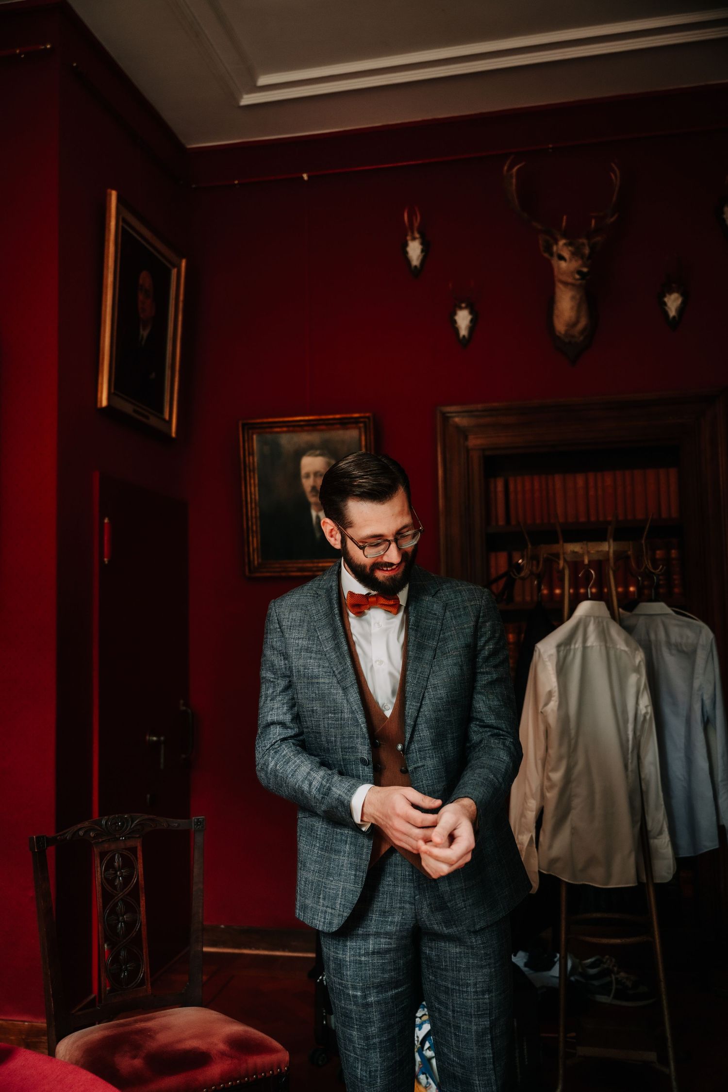 A moody scene in a red-walled room shows someone in a plaid suit jacket adjusting their attire.