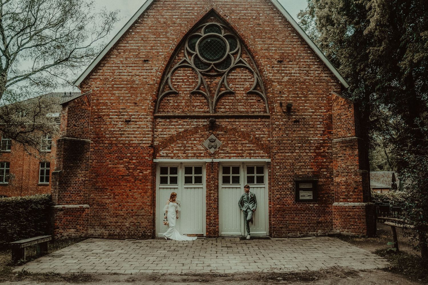 A historic red brick church building with gothic architectural details and white trim windows in a wooded setting.