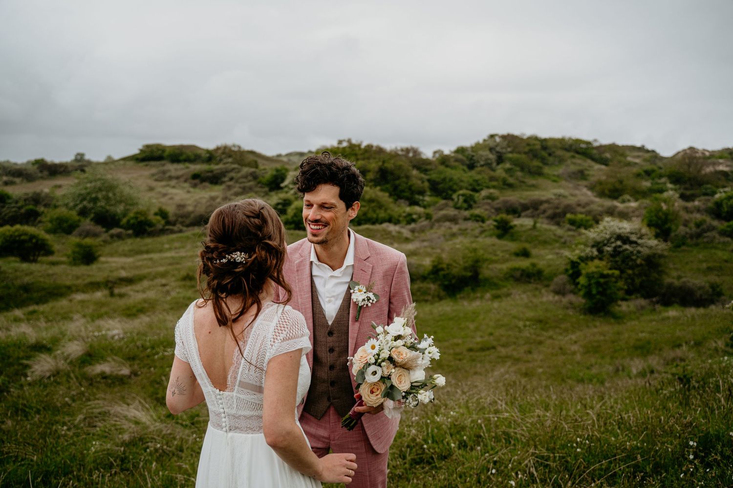 A couple poses together in a field with rolling green hills in the background.