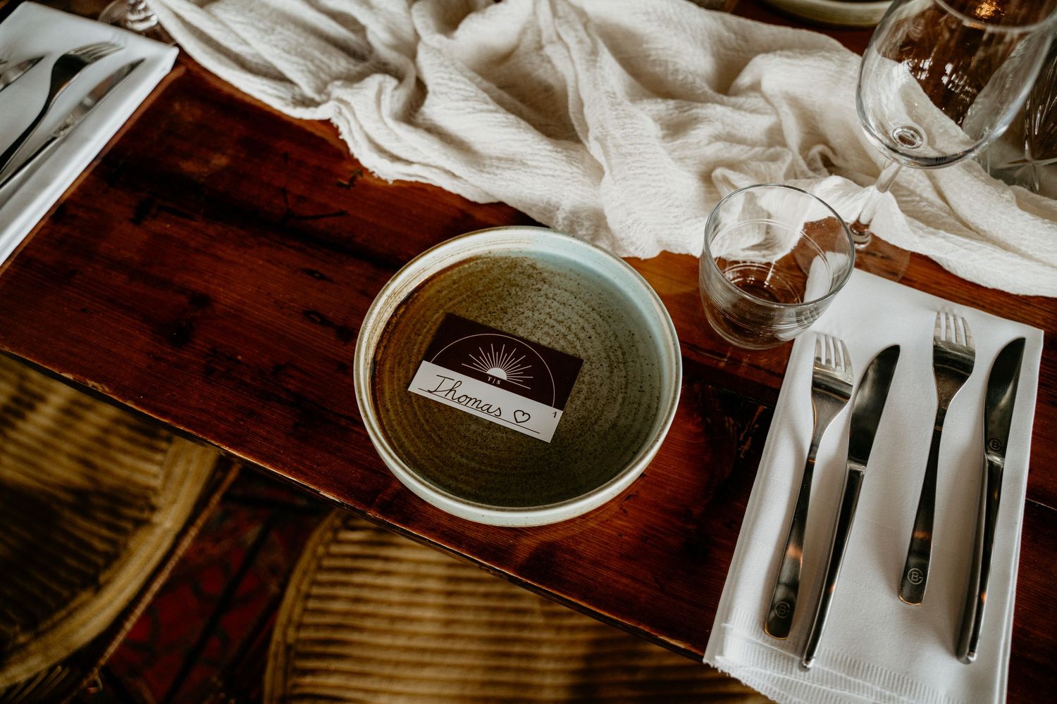 Place setting on wooden table with white linens, silverware and ceramic bowl.