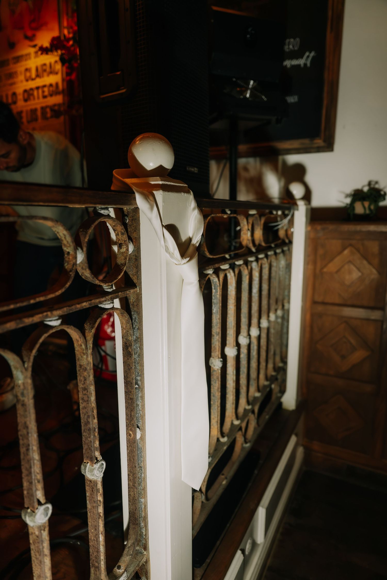 White wedding tie draped over ornate vintage iron railing inside elegant venue with warm lighting.