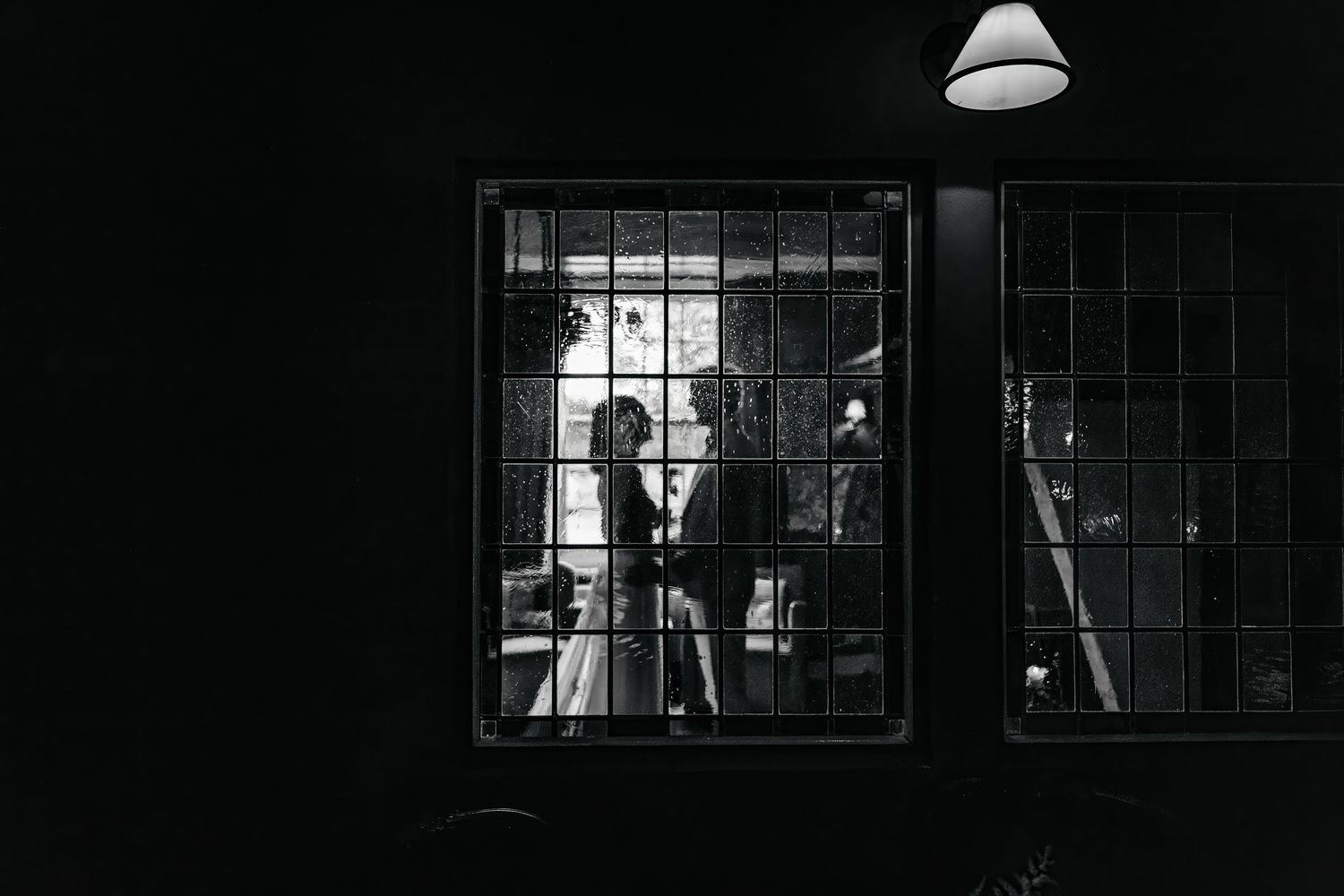 Row of lit windows in darkness with silhouettes visible through windowpanes.