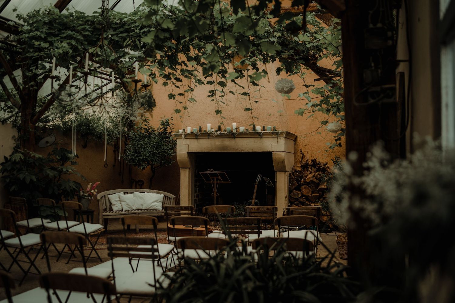Empty folding chairs arranged in rows facing a rustic fireplace in an outdoor courtyard.