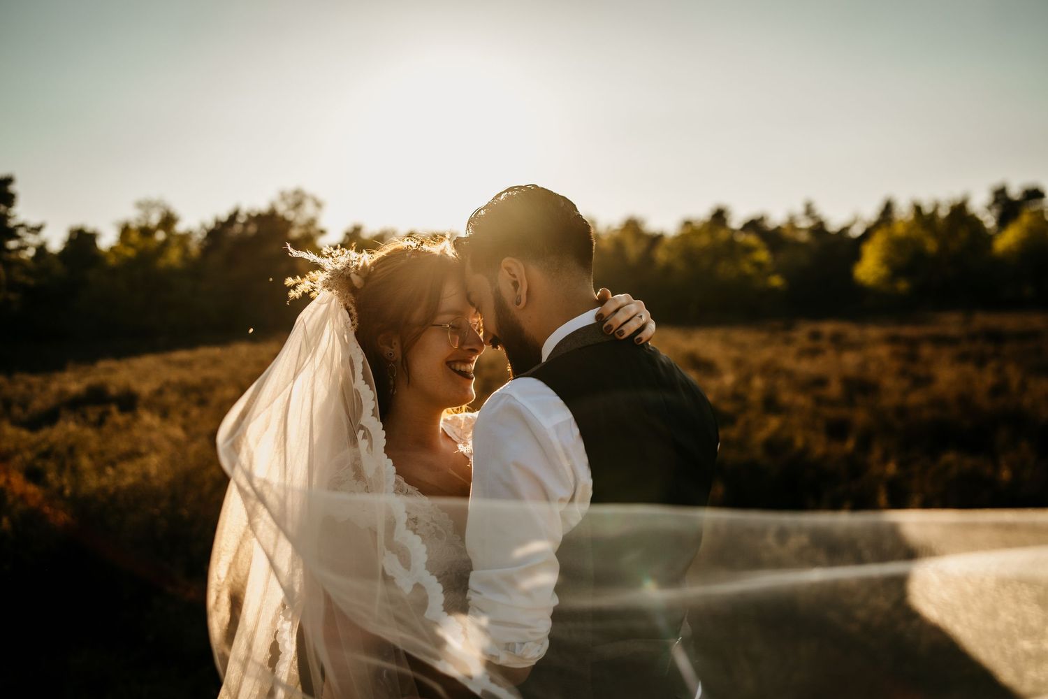 Romantic sunset wedding portrait with flowing veil in golden hour light.