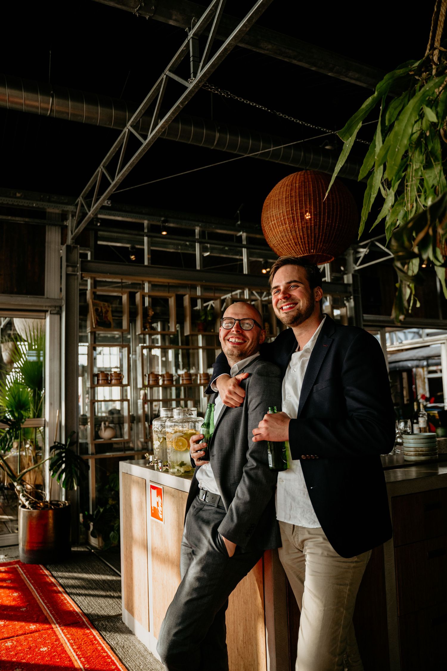 Two people share a candid moment in a modern restaurant interior with industrial design elements and hanging plants.
