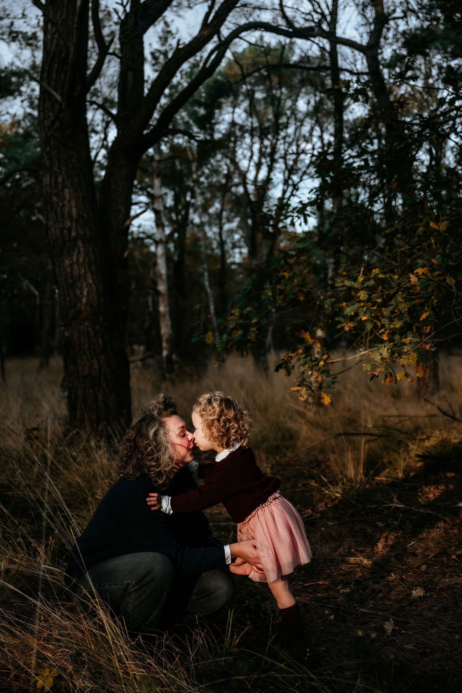 Romantic couple embraces in a wooded area during golden hour with autumn foliage.
