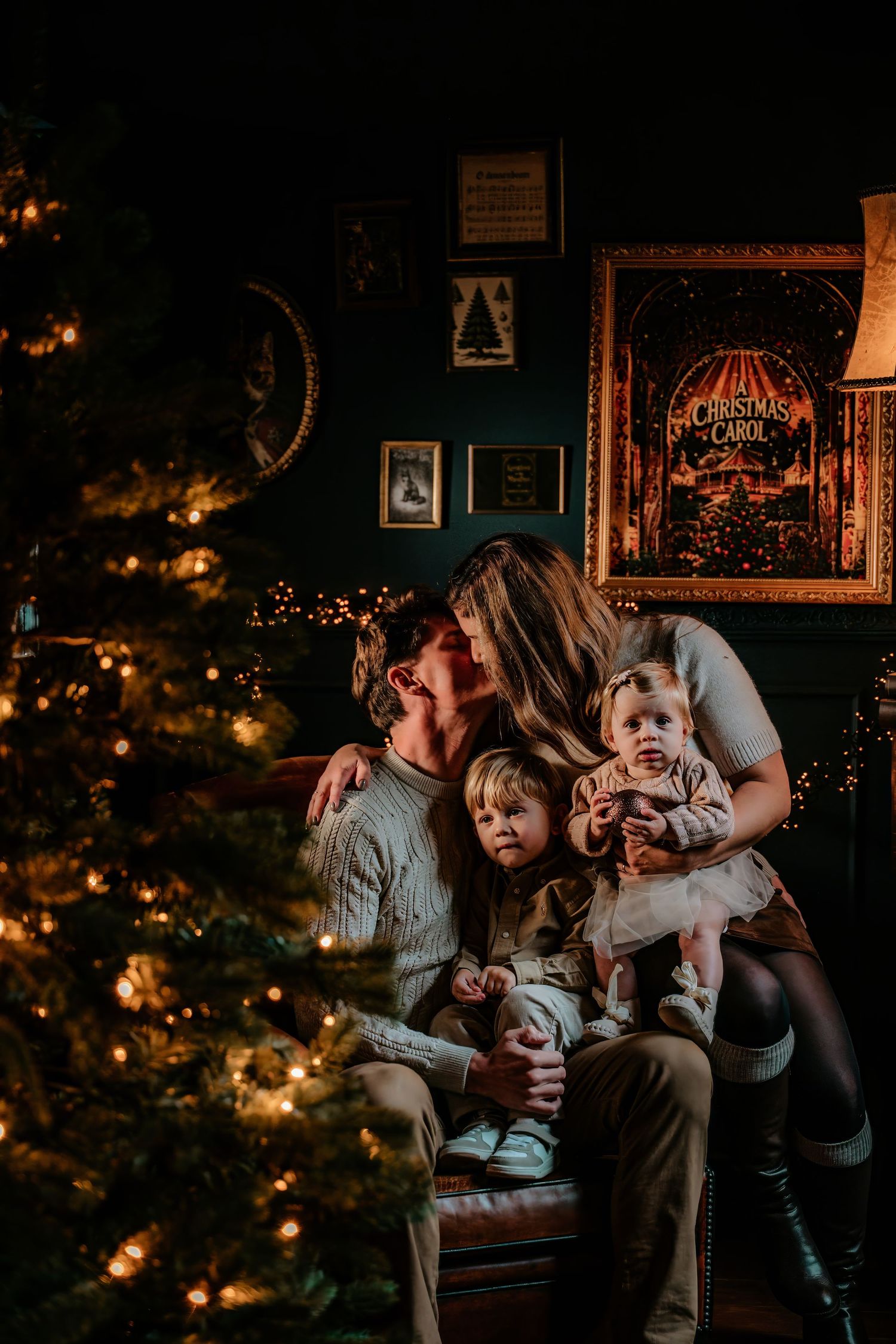 A family sits together by a glowing Christmas tree in a cozy living room with warm lighting and holiday decorations.
