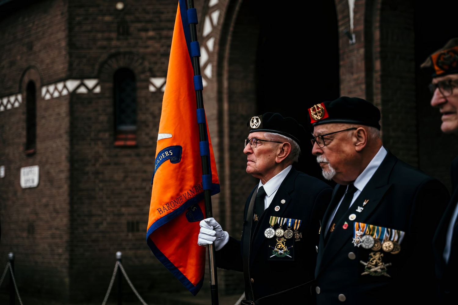 Military veterans stand in formation holding orange flags during a ceremonial event.