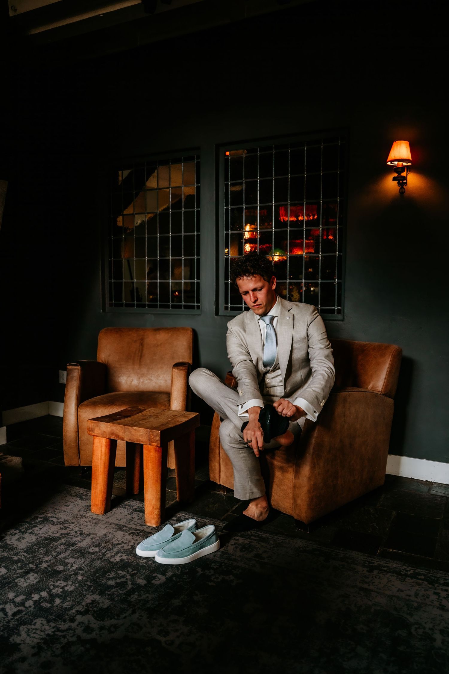 A grey suited figure sits alone in a leather chair preparing for an event.