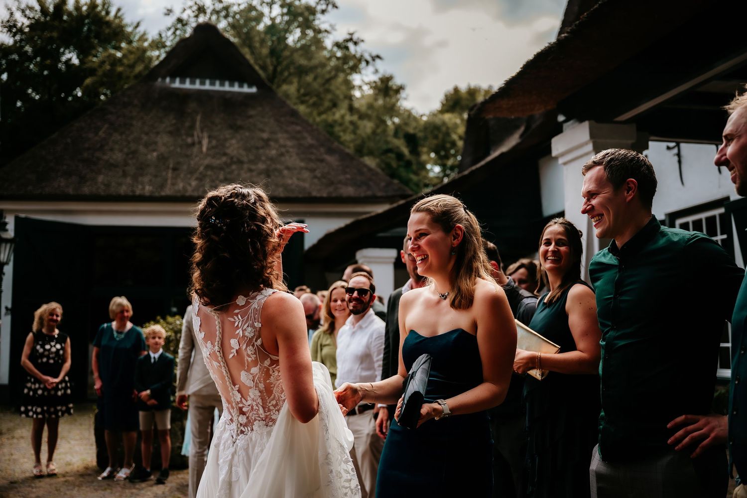 Wedding guests gather outdoors near a rustic building during a celebration.