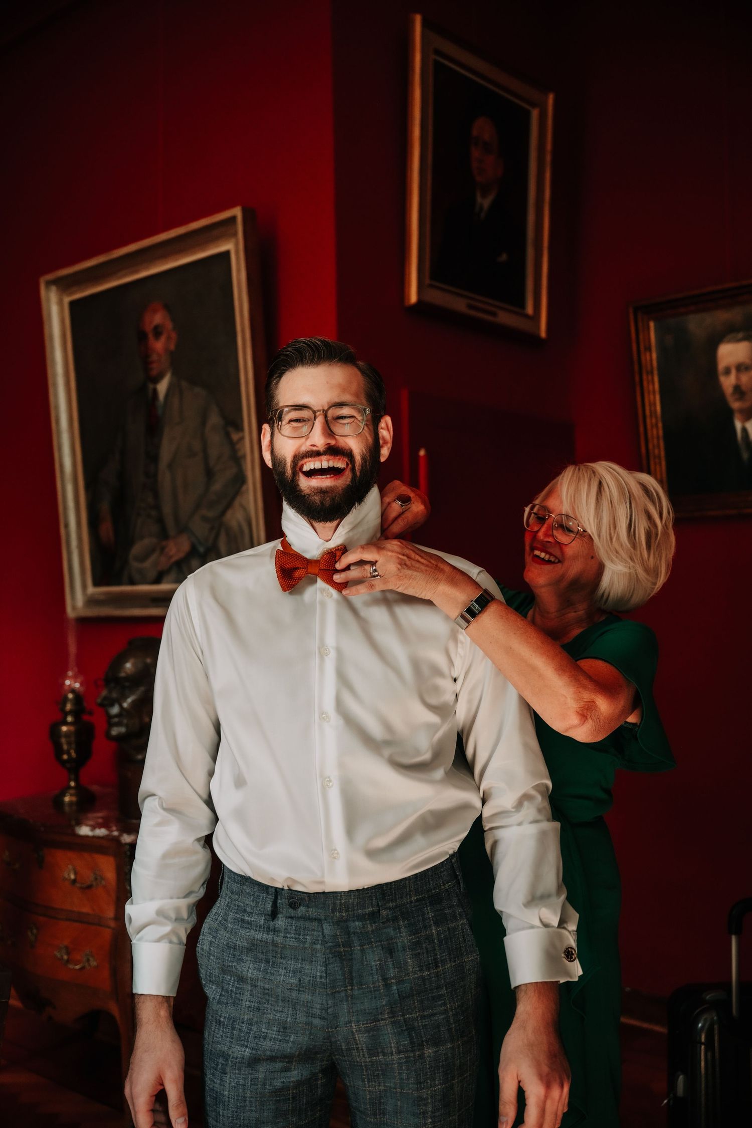 Candid moments during wedding preparations in a dimly lit room with red walls and vintage decor.