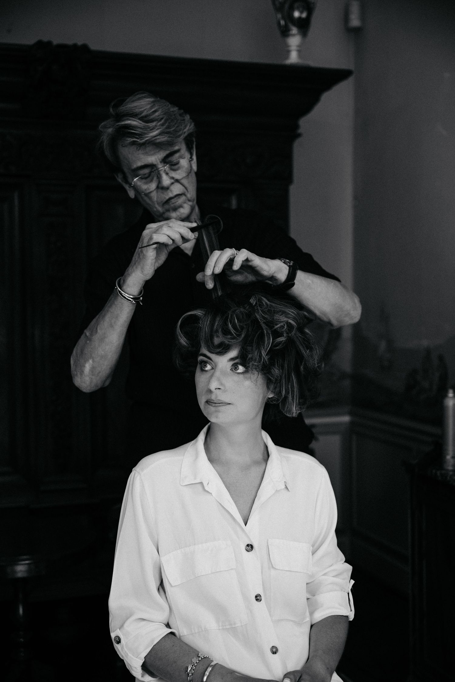 A stylist works on arranging a client's short dark hair in an elegant salon setting.