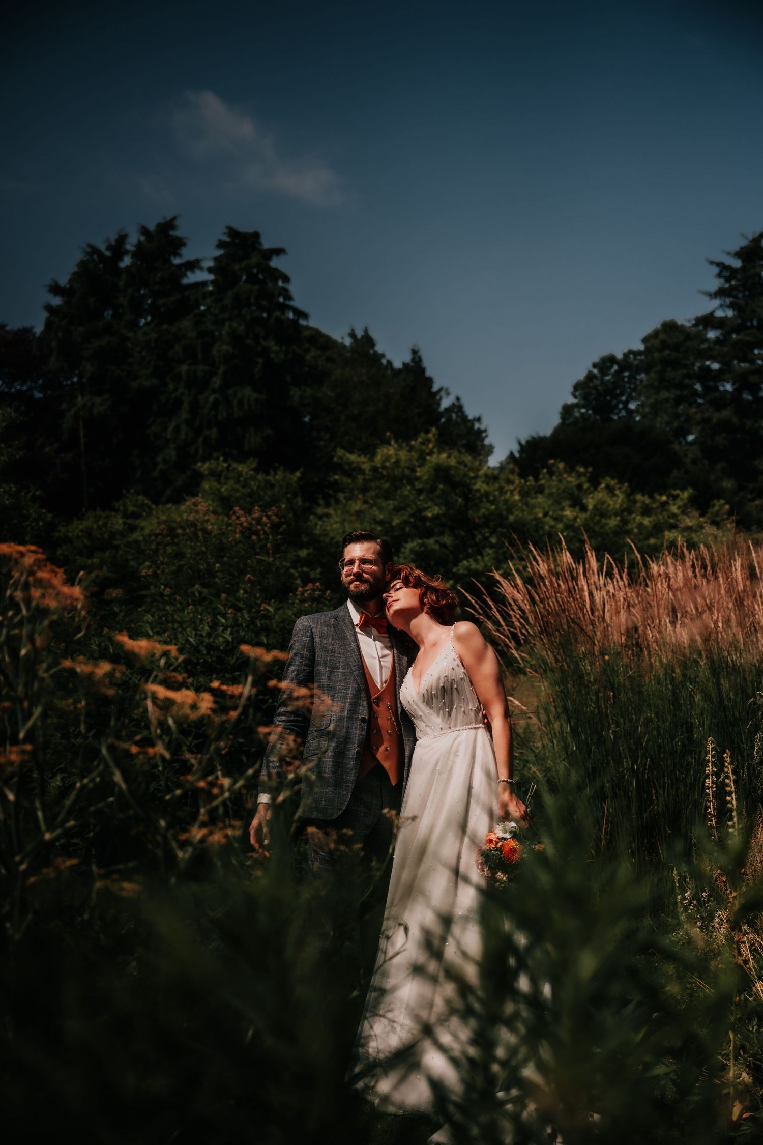 Romantic wedding couple embracing in tall grass during golden hour sunset.