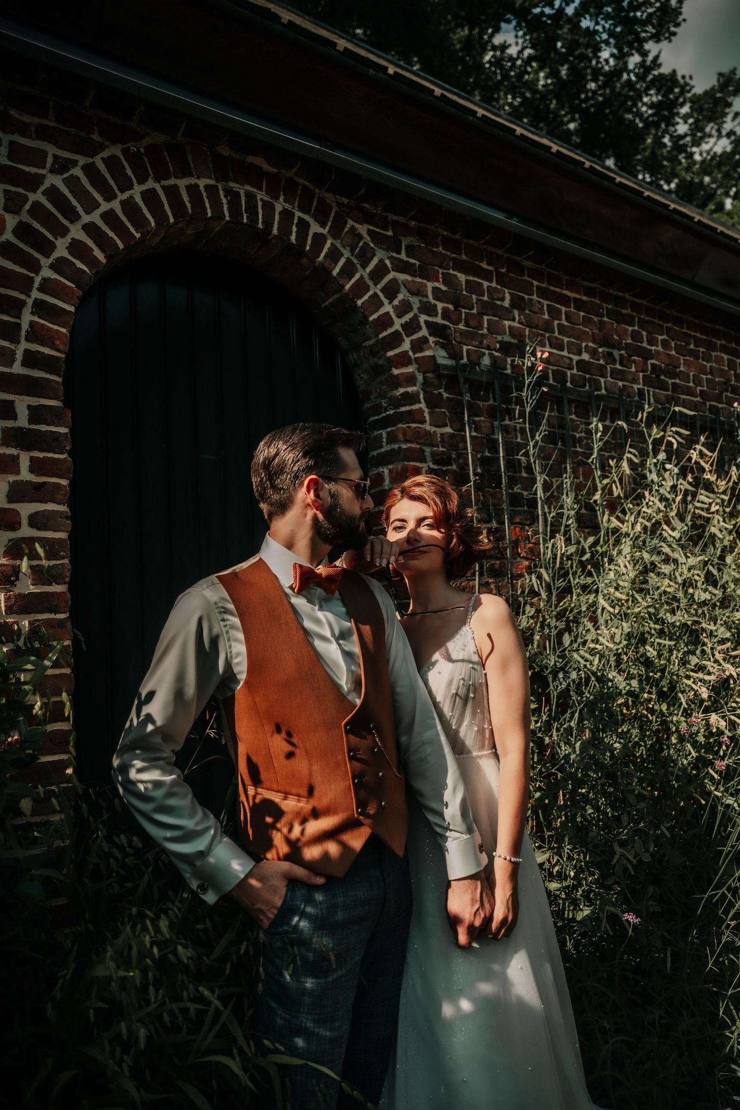 A tender embrace between newlyweds in front of a brick wall with greenery.