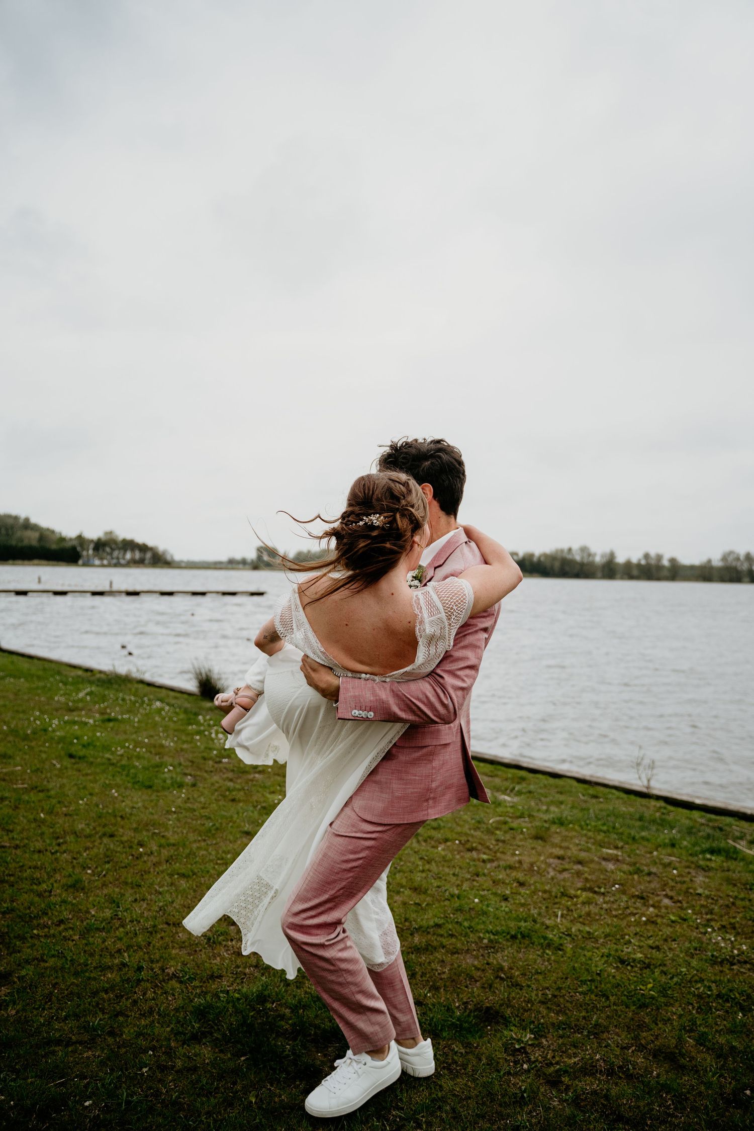 A romantic moment between newlyweds dancing by a lake with the bride's dress flowing in the wind.