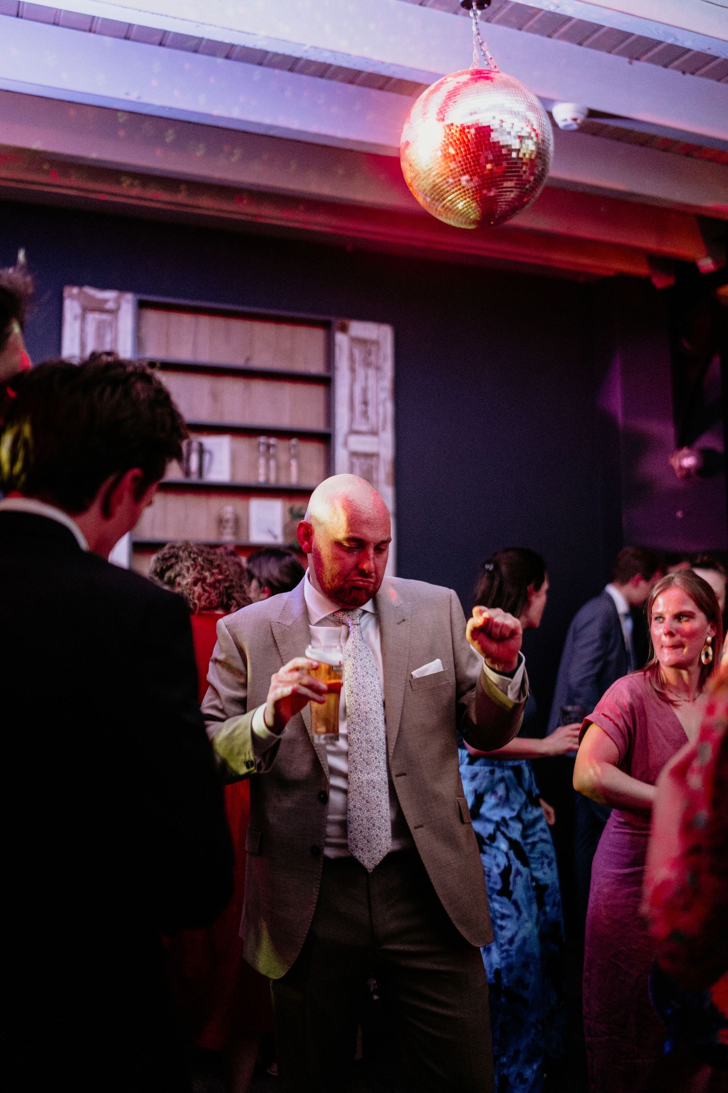 A celebration scene with a disco ball and guests enjoying drinks under purple lighting.
