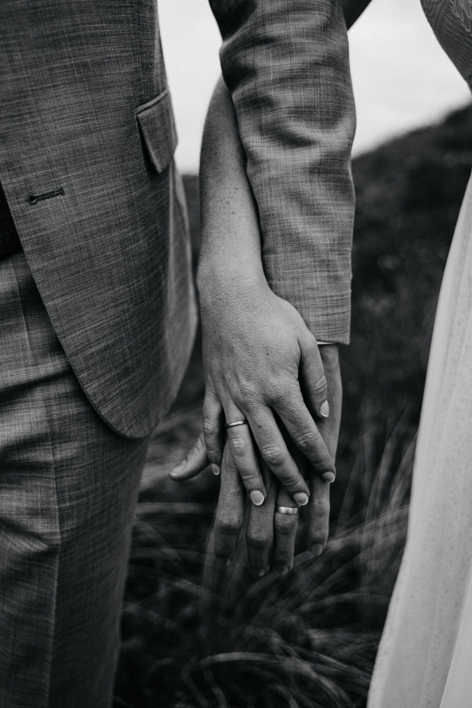 Close-up of hands wearing wedding rings against a dark background.