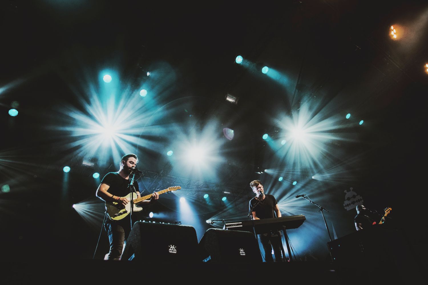 Concert stage illuminated with bright blue spotlights creating dramatic silhouettes of performers and equipment.