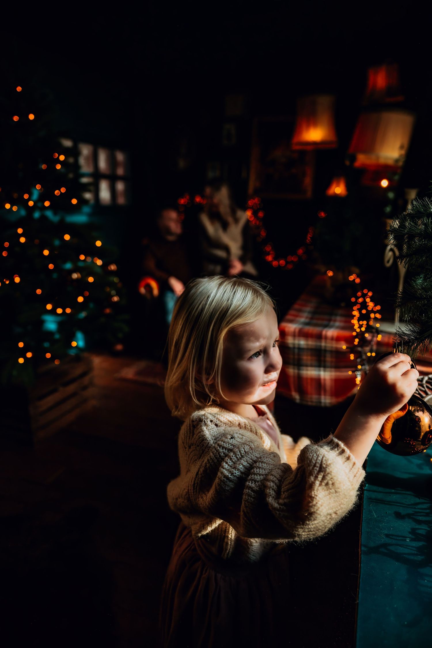 Person in cozy sweater illuminated by warm Christmas lights creates dreamy holiday atmosphere in dark room.
