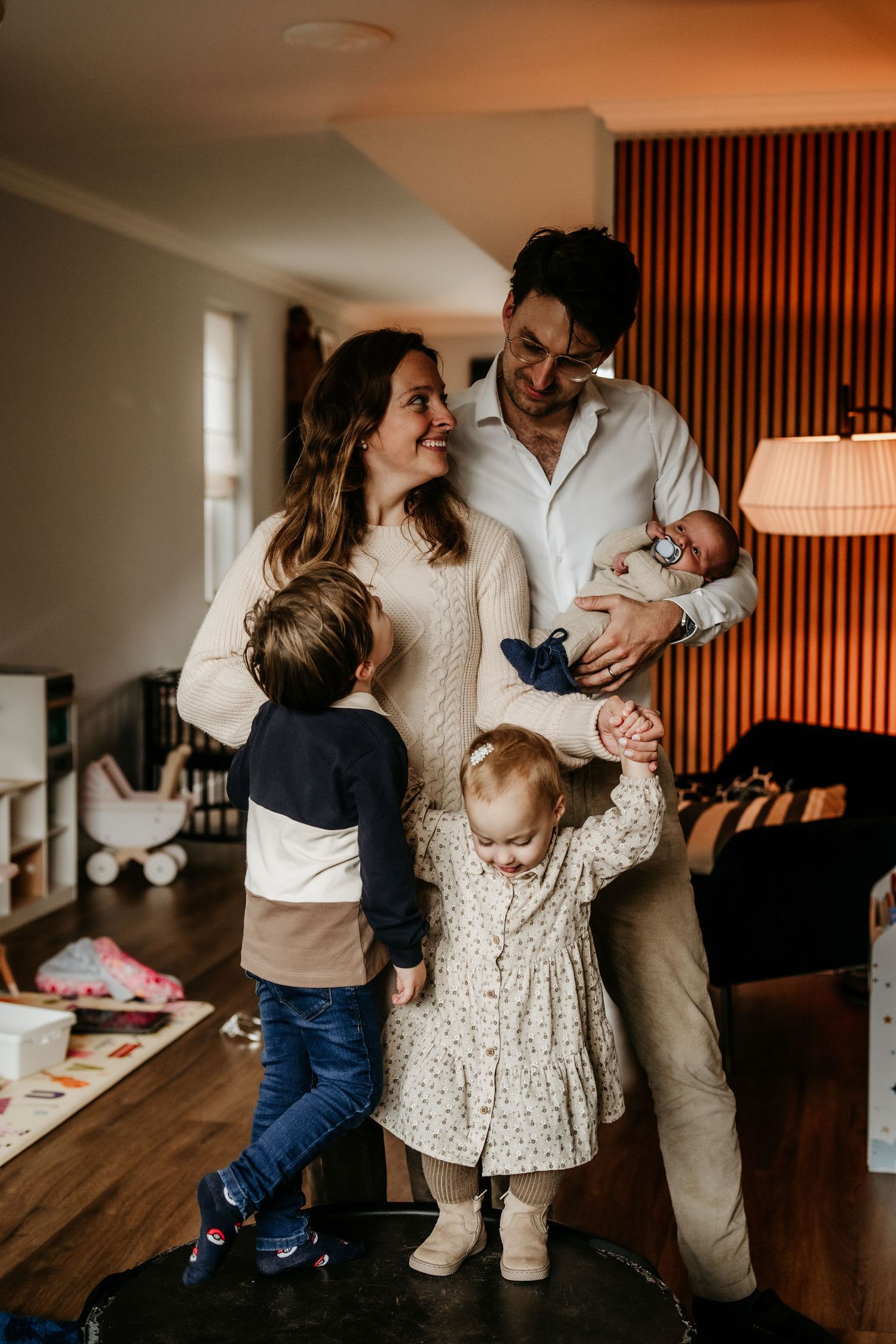 Family portrait with young children in cozy living room with warm lighting and modern decor.