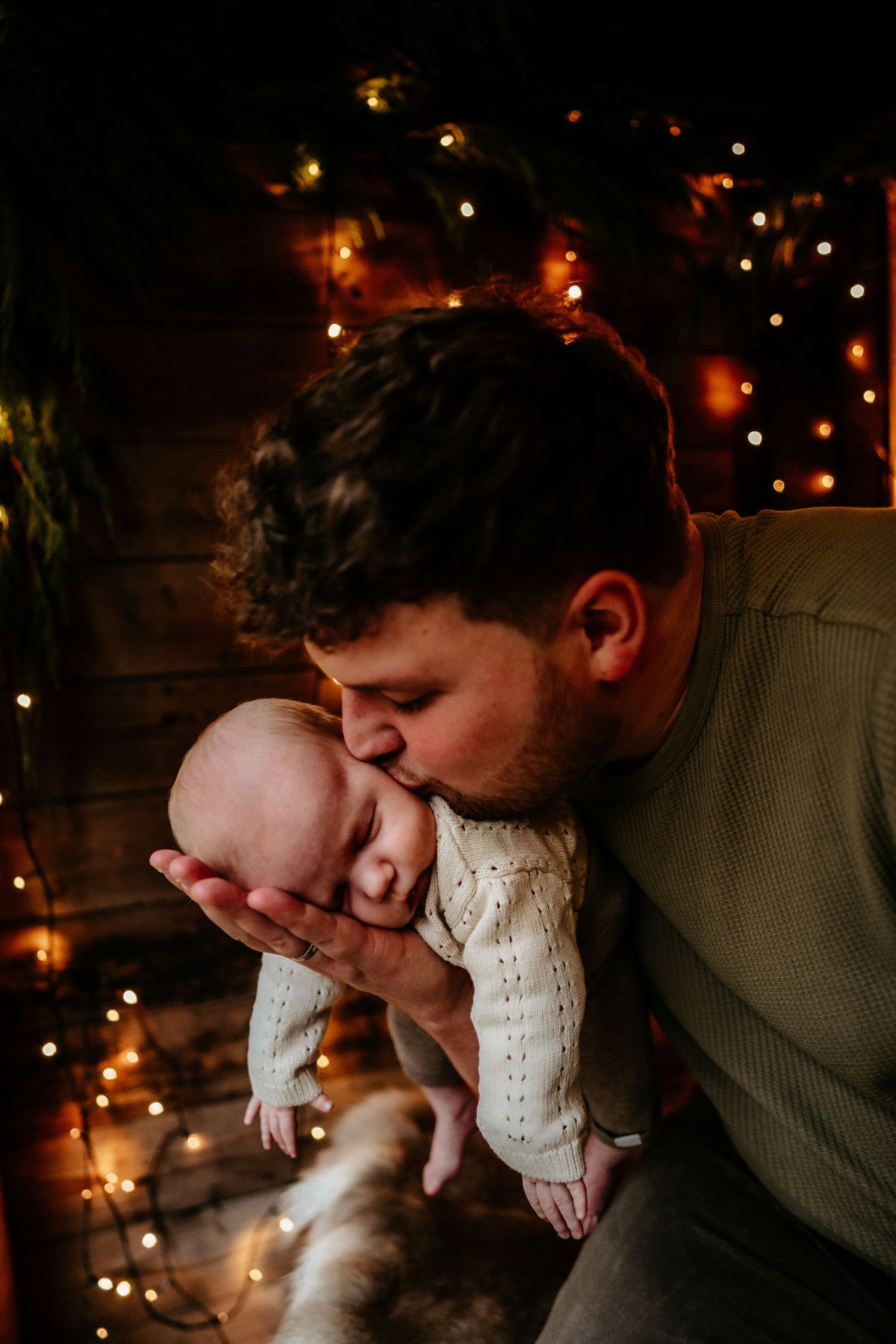 Intimate moment between parent and baby illuminated by soft Christmas lights.