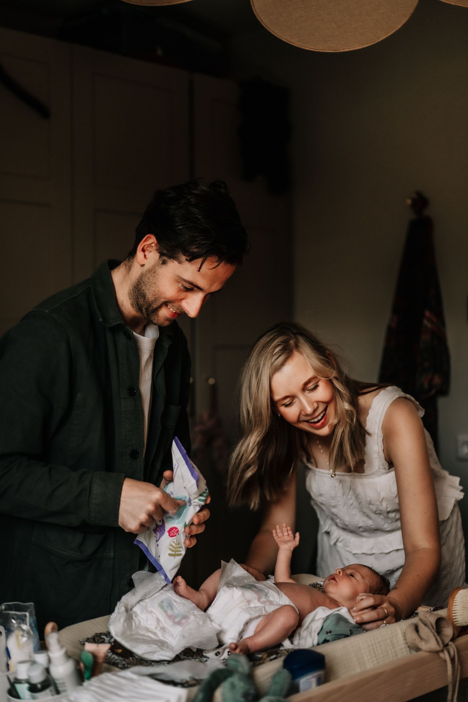 Family moment during a diaper change with crafting supplies scattered on table.