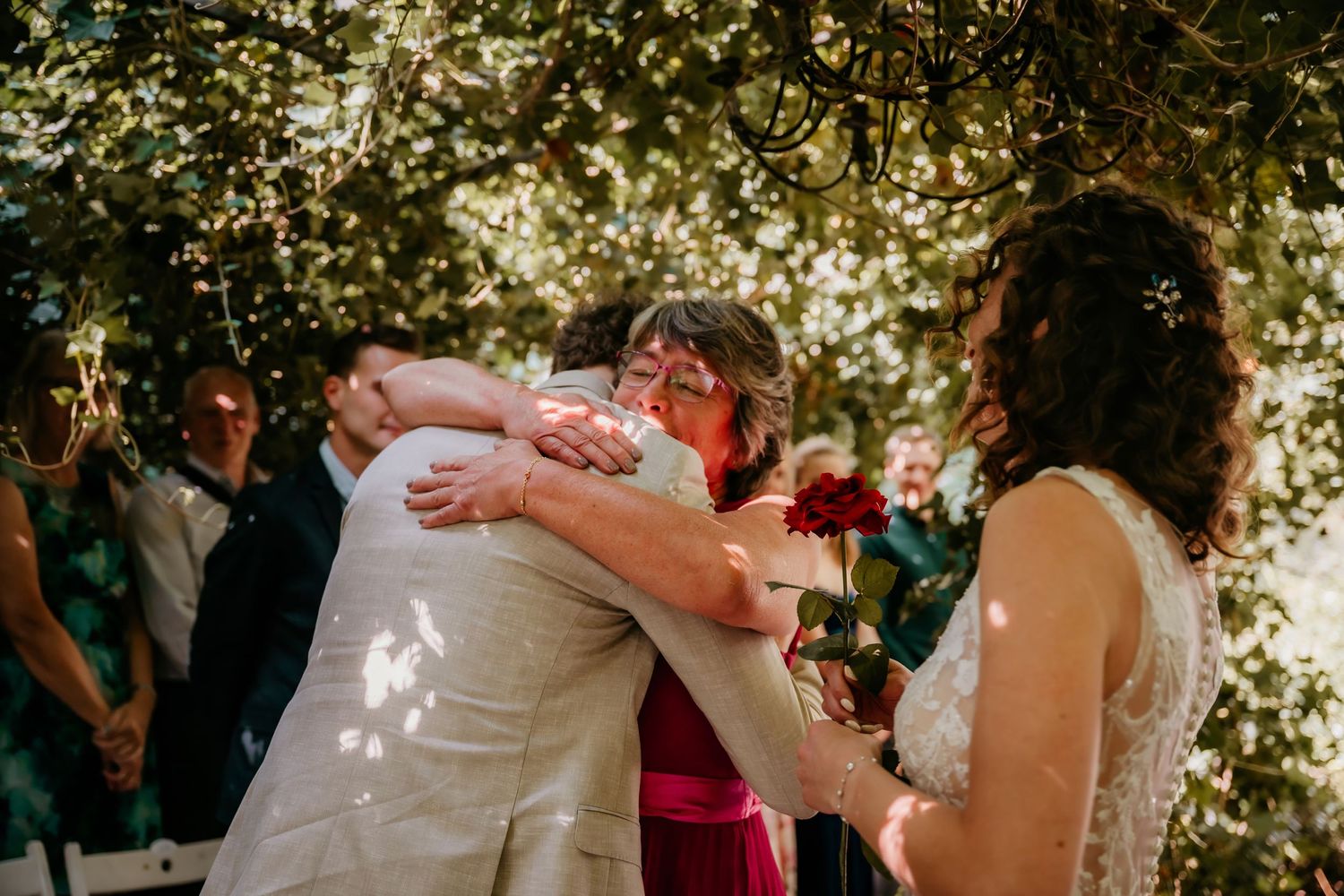 Outdoor wedding reception with guests dancing under dappled sunlight and trees.
